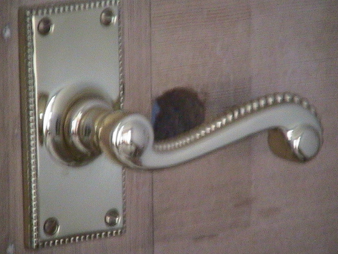 Een moderne deurklink met chromen afwerking en een gebogen hendel op een rechthoekig schild met een decoratieve rand.